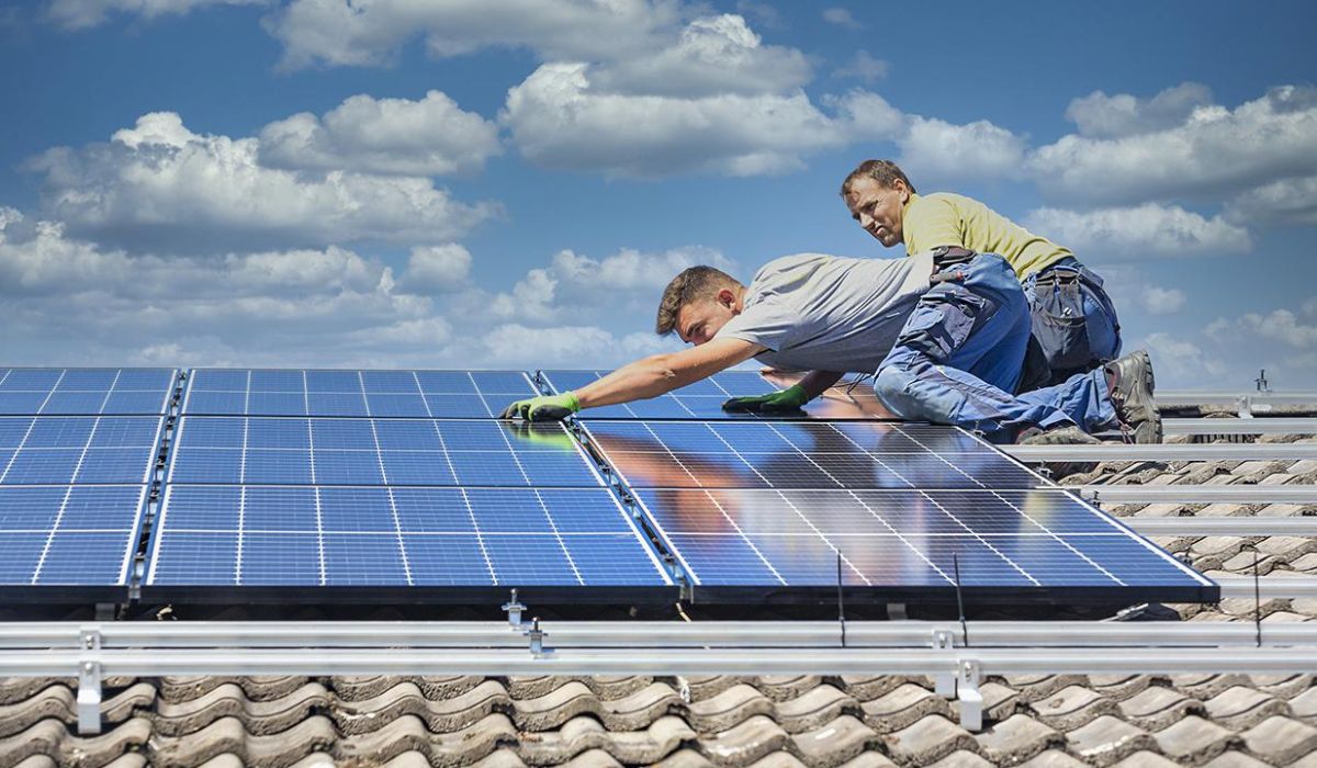 two roofing professionals installing solar panels on top of a roof