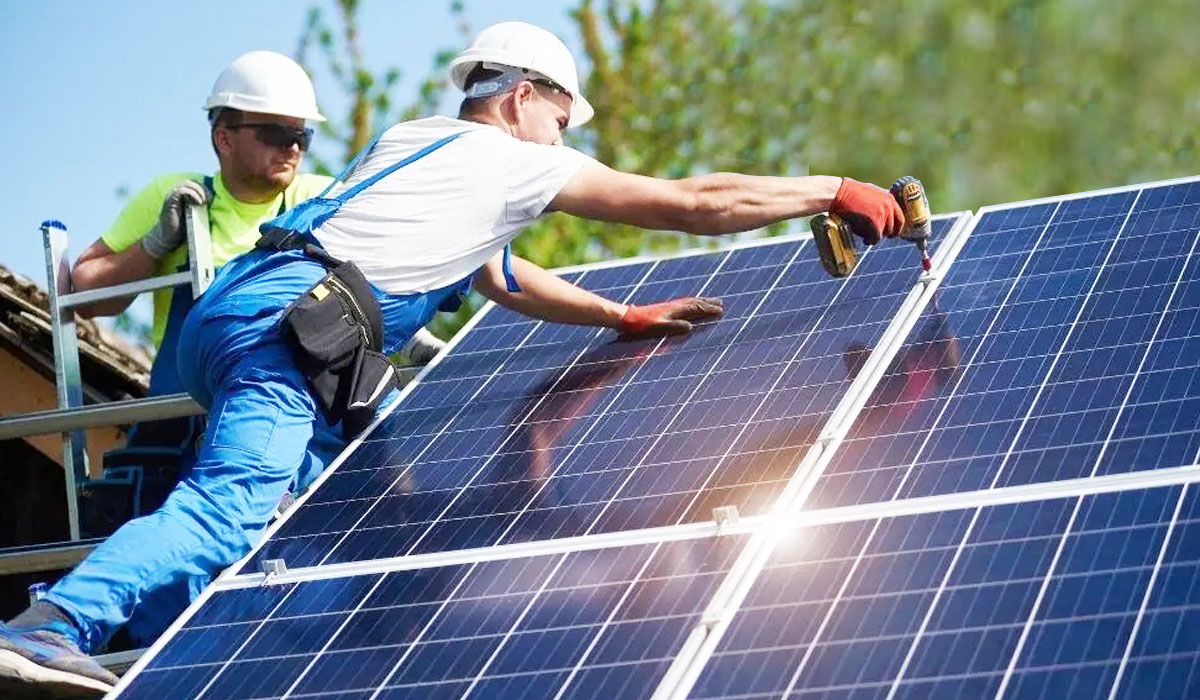 two men wearing hard hats installing solar panels on top of roof